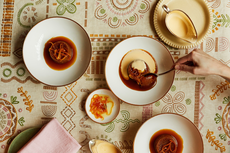 An image from above of three bowls of sticky toffee pudding desserts in mythical creatures crockery at Brumus restaurant, Haymarket Hotel. 