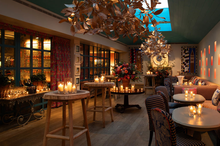 Close shot of a warm candlelight, floral decor, and gold leaf chandeliers at Orangery private events room at Warren Street Hotel