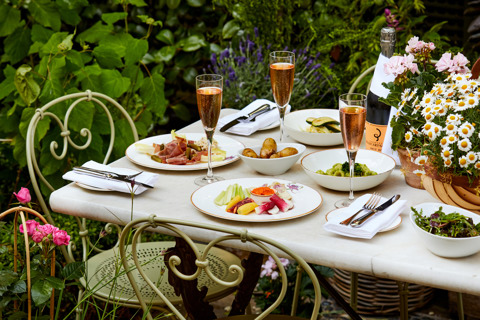 A wide shot of a table of starters in the garden at The Orangery. Plates of crudites, salad, pasta and ham with Champagne