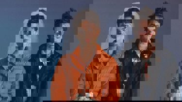 A still from the film "The Drama": A couple sit beside each other, the women to the left wearing an orange coat and wedding veil, the man to the right wearing a black coat