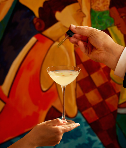 A close-up portrait shot of the non-alcoholic cocktail 'Mural You Look' at Oscar Bar & Restaurant: the cocktail is being held in front of the mural