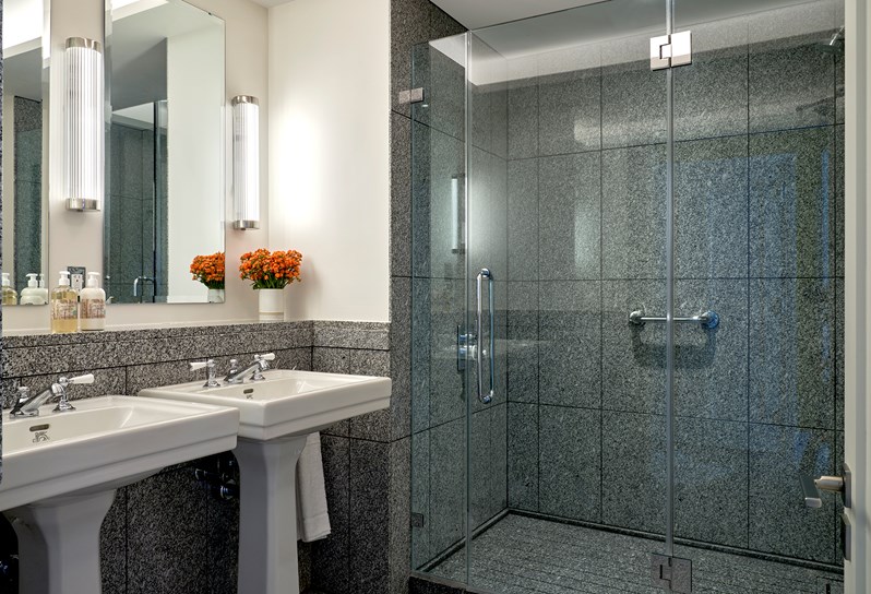 A granite bathroom. Two sinks stand in front of mirrors on the left hand wall. Behind there is a walk in shower.