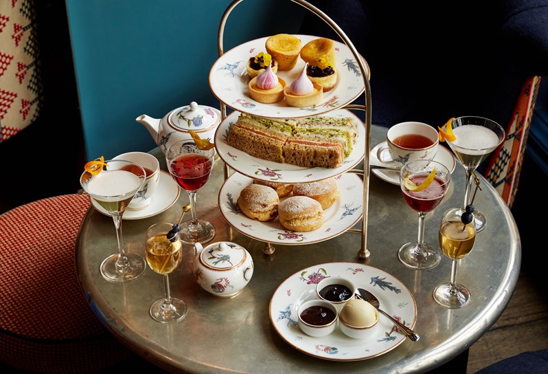 An image of the Afternoon Tea with a Twist at Oscar, Charlotte Street Hotel. The table displays the afternoon tea set up and cocktails.