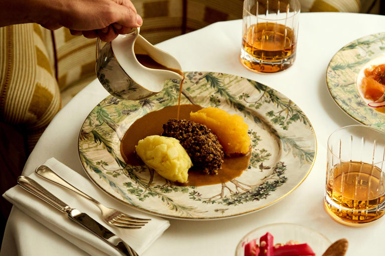 A plate of haggis, neeps and tatties with gravy being poured over it, with a glass of whisky, for Burns Night dinner with Bruichladdich at Covent Garden Hotel