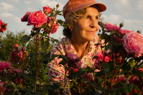 Florist Rosebie Morton seen crouched within a flower bush with the sun shining on her