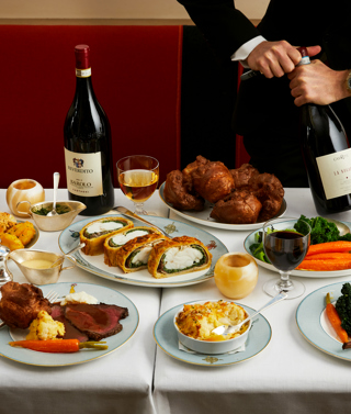 The Long Lunch at Ham Yard. A large table with three magnums of wine, sharing plates of meat and sides of potatoes, vegetables and cauliflower cheese