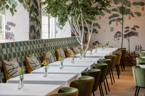 Refuel Cafe at Treasure House Fair. A shot looking down a row of tables in front of banquette seating upholstered in a green patterned fabric with green dining chairs opposite