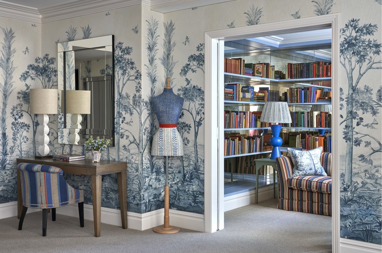 A diagonal shot looking into the alcove section of a Deluxe Junior Snug Suite at Ham Yard Hotel. Next to a writing desk and mannequin, double sliding doors open up to reveal a sofa and bookshelves