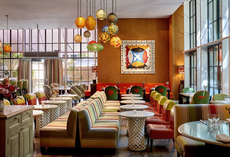 View of the Crosby Bar from the restaurant side with the bar tables and their sofas and low chairs in a straight line facing the angle and another line parallel to it on the left. The curtain walls can be seen at the back and on the right of the picture.