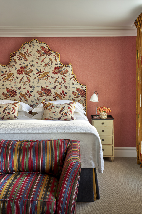 A portrait image of Accessible Deluxe Junior Suite, 203, Charlotte Street Hotel. It shows an image of the bed from the foot showing the sofa at the end as well as the headboard in a autumnal colour scheme.