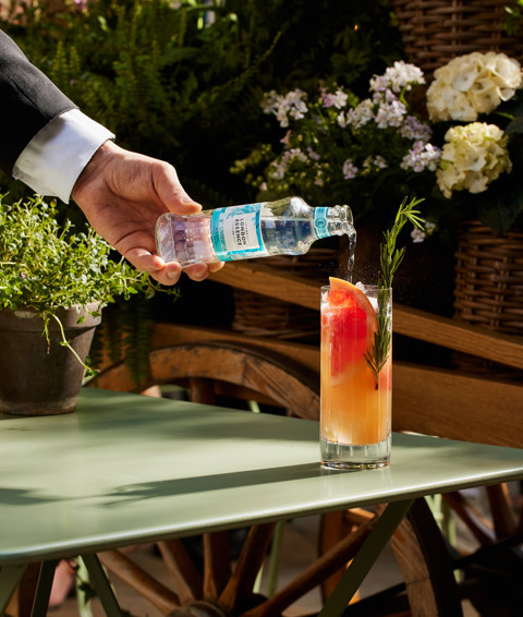 A close-up portrait shot of one of the Wimbledon cocktails at Ham Yard Bar & Restaurant being served on a table in the courtyard: the London Essence tonic is being poured into the cocktail.