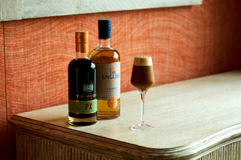 An image of a brown, smoky cocktail, frothy on top. Next to a bottle the The English Smokey whiskey and The Norfolk PX.