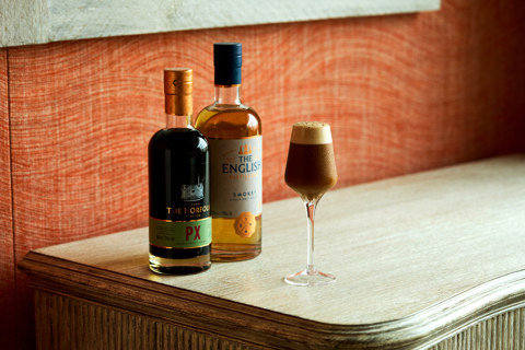 An image of a brown, smoky cocktail, frothy on top. Next to a bottle the The English Smokey whiskey and The Norfolk PX.