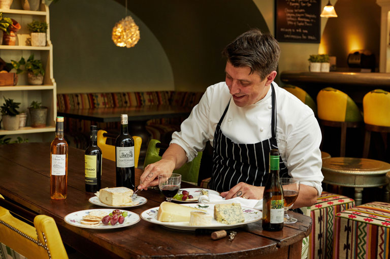 A image of Joe Fox at a table with multiple different plates with cheeses and wine at The Potting Shed, Dorset Square Hotel. 