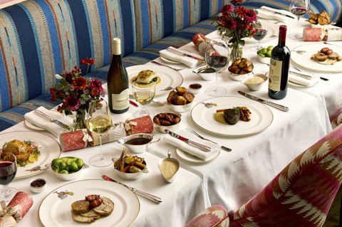 A table of six set up for Christmas dining at Brumus. There are plates of meat and fish with small side dishes and bottles of wine