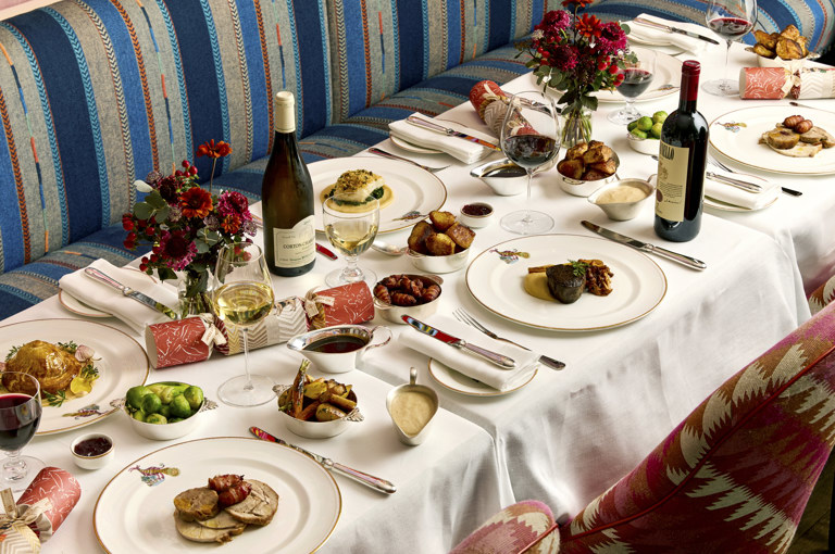 A table of six set up for Christmas dining at Brumus. There are plates of meat and fish with small side dishes and bottles of wine