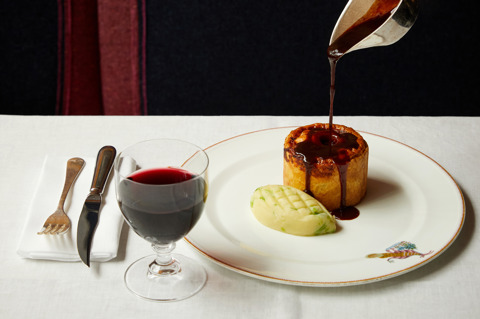 Gravy is poured over a main course of pie and mash on a plate with a glass of wine at Brumus
