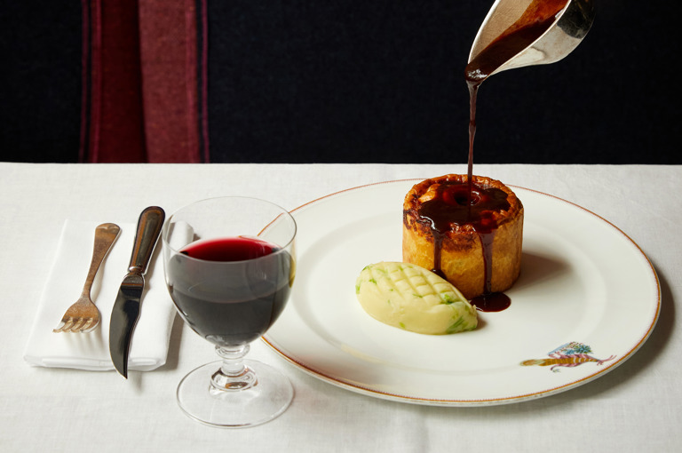 Gravy is poured over a main course of pie and mash on a plate with a glass of wine at Brumus