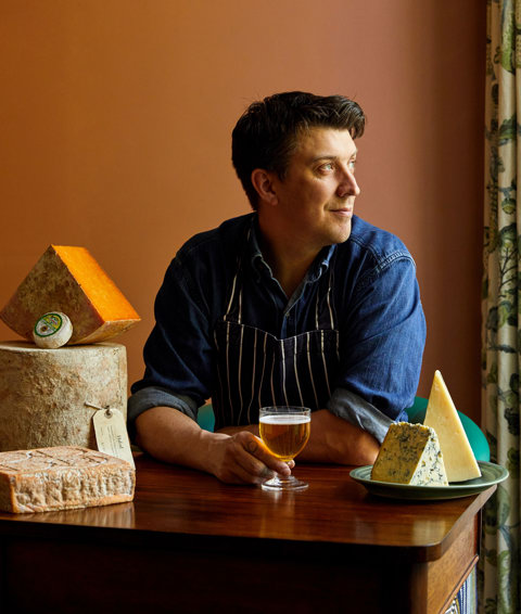An image of Joe Fox holding a glass of beer surrounded by different cheeses at The Potting Shed, Dorset Square Hotel. 