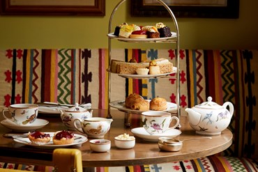 Afternoon tea displayed on a table in The Potting Shed restaurant at the Dorset Square Hotel. The fine bone china is Mythical Creatures by Kit Kemp for Wedgwood along side a 3 tier cake stand, sandwiches and scones.