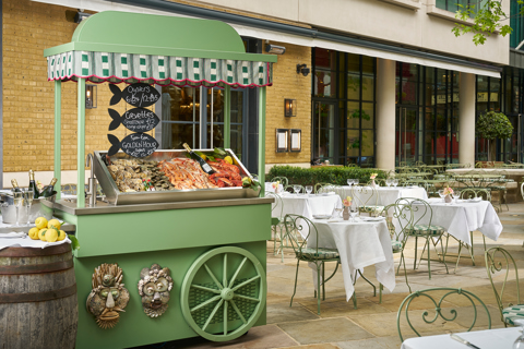 Wide shot of the exterior of Ham Yard Hotel featuring a green oyster cart and tables set up for outdoor dining
