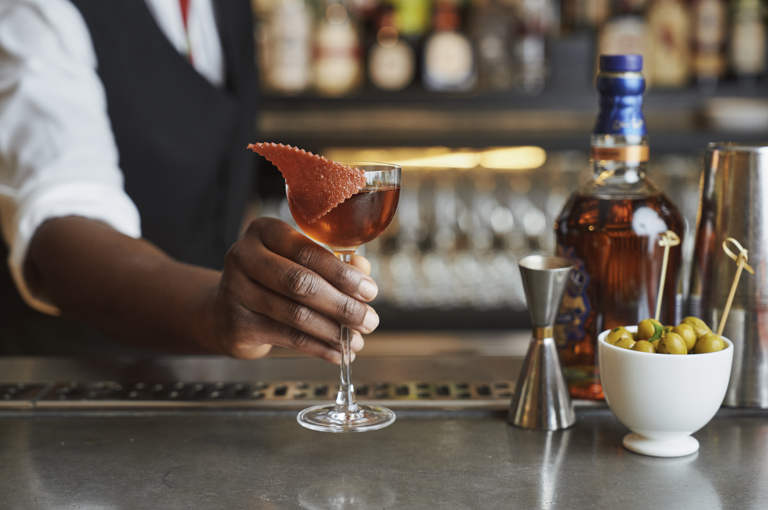 Wide shot of a bartender presenting a cocktail on the bar at Ham Yard
