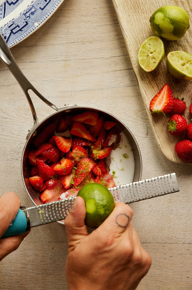 A close-up portrait shot of the process of making the strawberry and lime meringue roulade: the strawberry compote is being made with lime zest