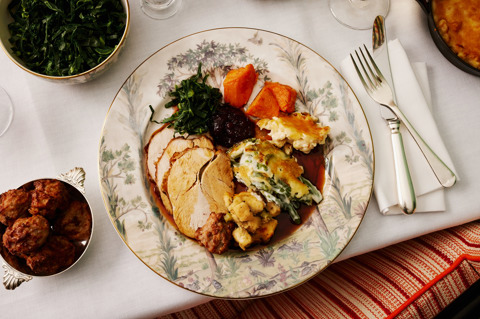 This image is to promote Brasserie Max's Thanksgiving menu at Covent Garden Hotel. It shows a close up of a traditional turkey dish with roast vegetables, baked greens and gravy, served on Tall Trees crockery with wine, candles and pumpkins on the table.