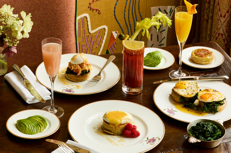 A wide shot of brunch dishes being served in the Dora Carrington Room at Charlotte Street Hotel: there are various dishes using crumpets as well as cocktails on the table