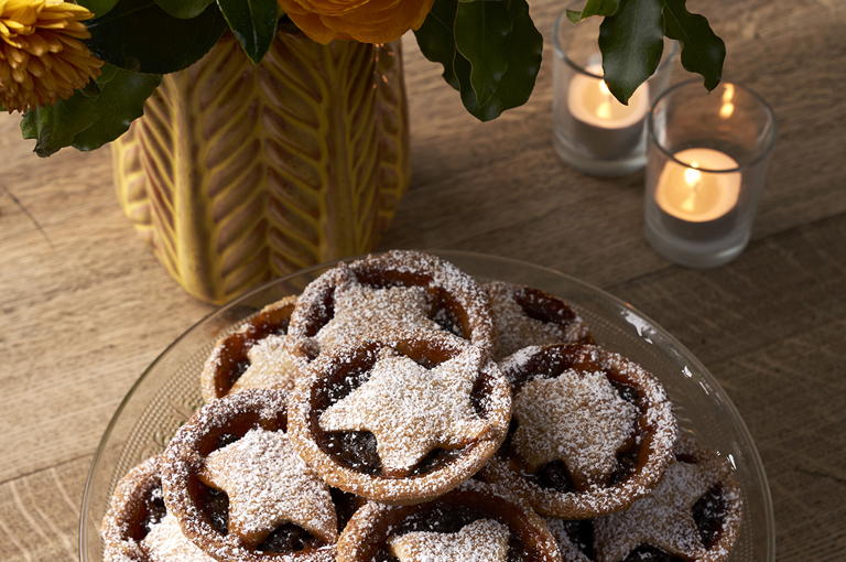A plate of homemade mince pies sit on a wooden table