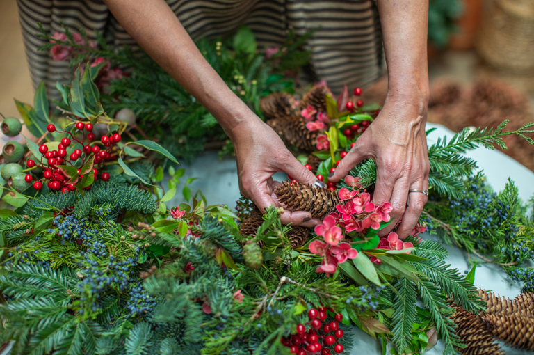 A close up shot of florist Tawana Schlegel creating a Christmas wreath with foliage and berries on a table at Warren Street Hotel