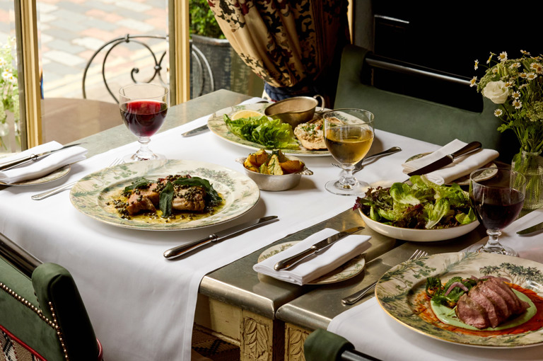 An image to promote Brasserie Max’s À La Carte menu at Covent Garden Hotel. The image shows a variety of dishes on the rectangular table and glasses of wine.