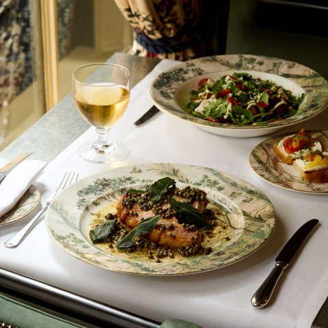 An image to promote Brasserie Max’s À La Carte menu at Covent Garden Hotel. The image shows a close up image table with focus on the sea bass and glasses of wine.