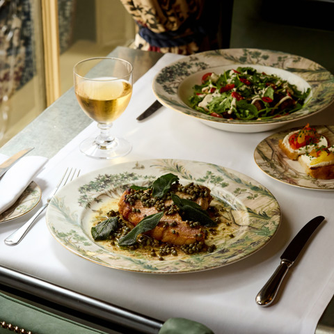 An image to promote Brasserie Max’s À La Carte menu at Covent Garden Hotel. The image shows a close up image table with focus on the sea bass and glasses of wine.