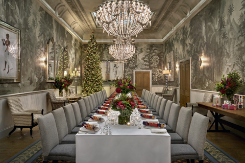 An image of a long dining festive table and a Christmas tree in the Shooting Gallery at Haymarket Hotel. The table displays dining set up with Mythical Creatures crockery, festive flower displays and crackers.