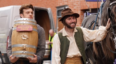 A still from the film "Mother's Pride", showing two men. One holding a barrel and one with his hand on a horse. 
