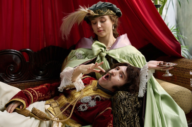A still from the film 'Madfabulous': the image portrays two people, dressed in 19th-century clothing, and the woman is feeding the man a date