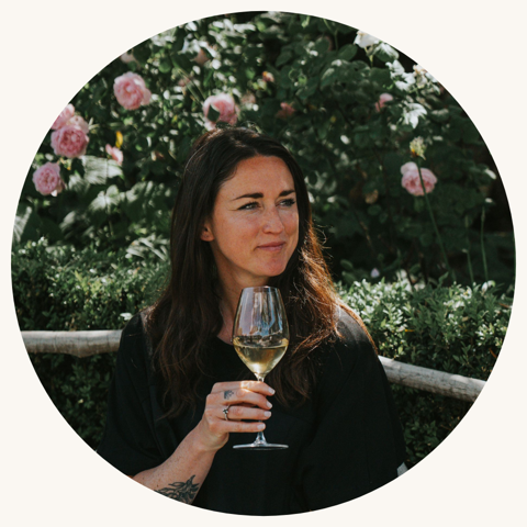 A portrait shot of Emily Harman (VinaLupa) sat on the roof terrace at Ham Yard Hotel, holding a glass of white wine against a floral backdrop.