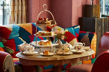 Afternoon tea displayed on a table in Brumus restaurant at the Haymarket Hotel. The fine bone china is Mythical Creatures by Kit Kemp for Wedgwood along side a 3 tier cake stand, sandwiches and scones.