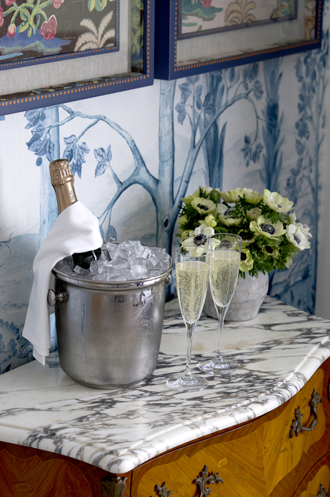 An ice bucket holding a bottle of Champagne alongside two Champagne glasses on a marble surface in a suite at Crosby Street Hotel