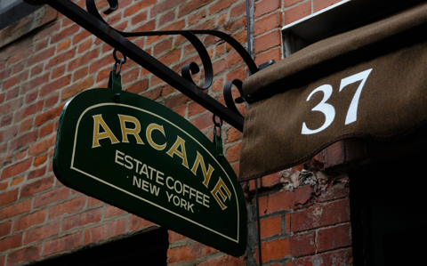 A sign for Arcane Coffee in New York hangs against the backdrop of a brick building