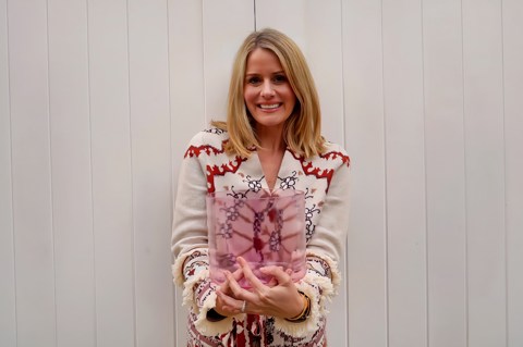 A shot of sound practitioner Nancy Trueman standing in front of a white wall smiling and holding a crystal bowl
