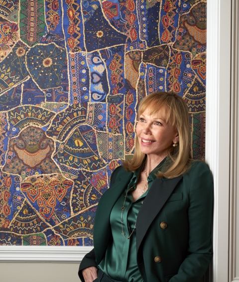 A portrait image of Kit Kemp in front of a wall covered in Kit Kemp x GP & J Baker's Front Row in Jewel Blue. In the image she is leaning against the wall looking to the left.
