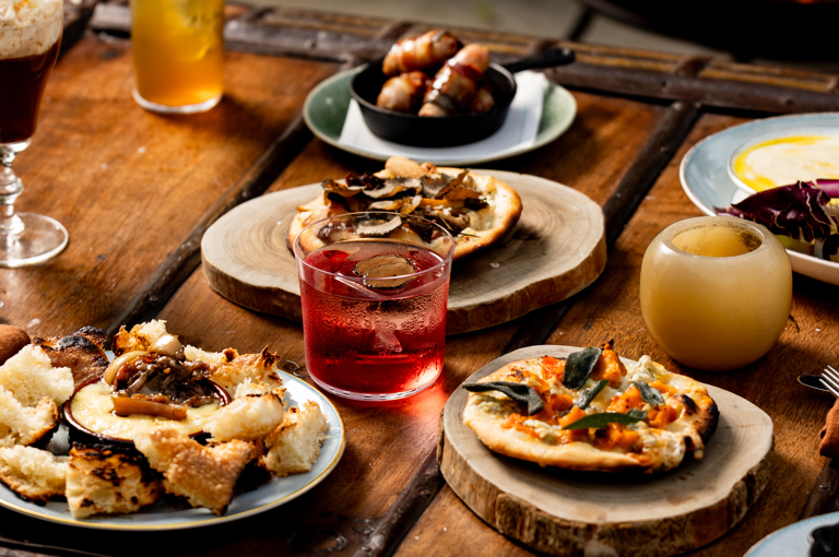 A selection of fire-cooked dishes and cocktails sit on a wooden coffee table