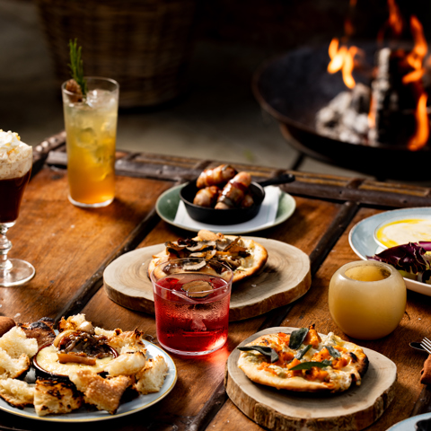 A selection of fire-cooked dishes and cocktails sit on a wooden coffee table