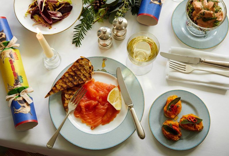 A closeup of the smoked salmon, toast bread and lemon starter that is served on a Sailor's fairwell plate. There is a small plate of pumpkin bruschetta, a plate of Autumn leaves salad as well as a prawn cocktail that is seen on the side. This is paired with a glass white wine.