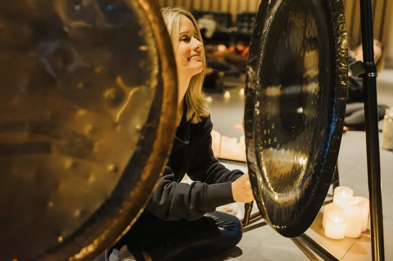 A close up shot of sound practitioner Nancy Trueman sitting in front of two gongs 