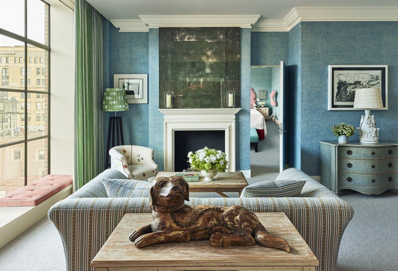 A blue themed sofa facing a fire place with a mirror above.