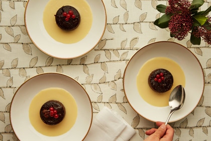 Wide shot of a festive table with Christmas Puddings and a hand reaching for it