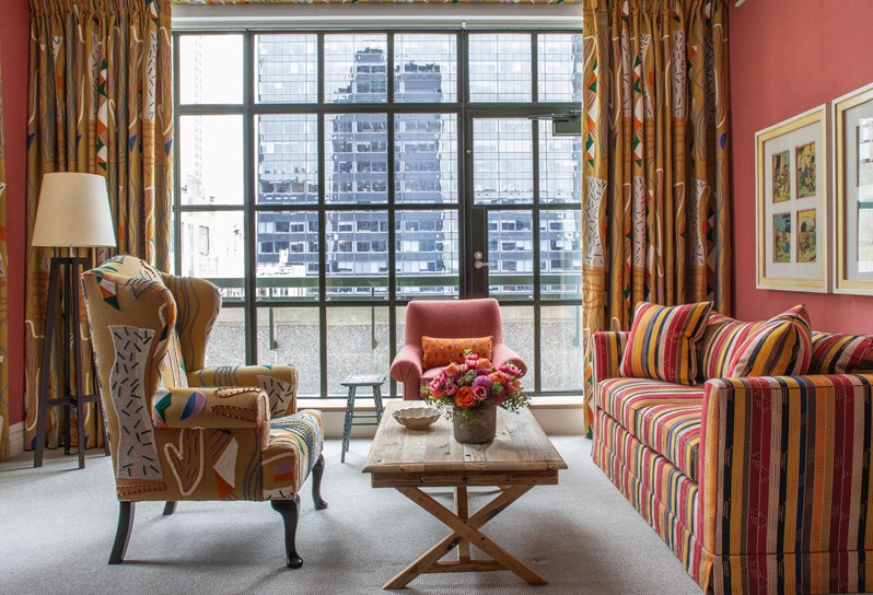 A large, whimsical living room with inviting lounge furniture and bold colors looking over a floor to ceiling Crittall windows